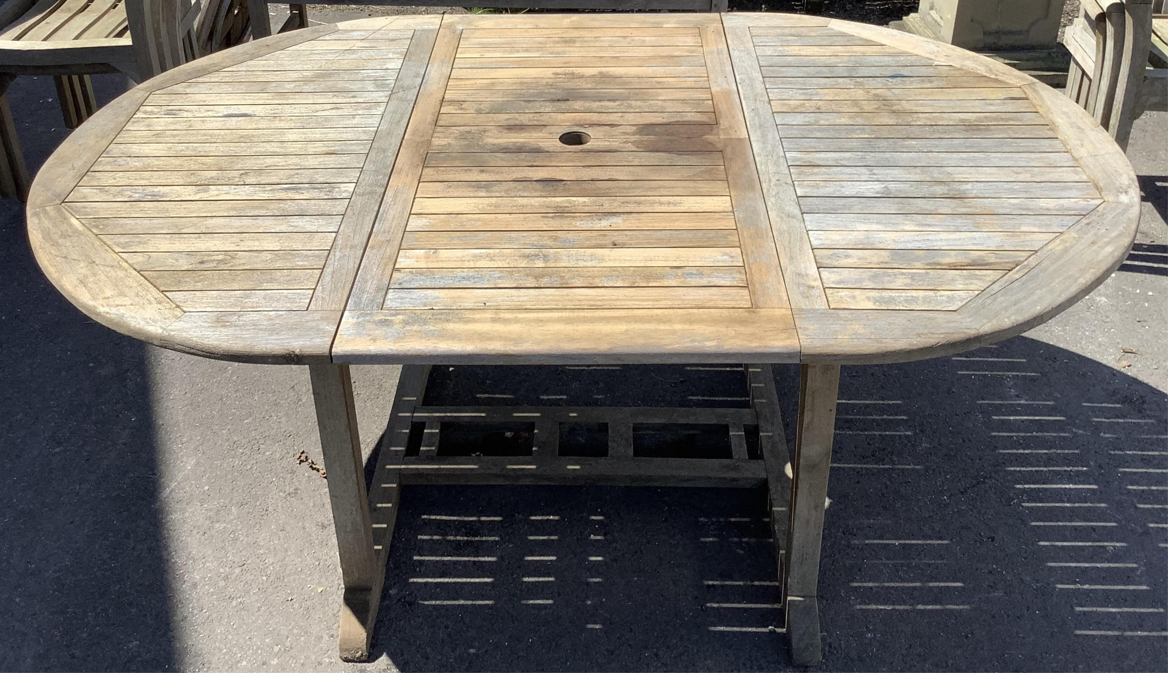 Six Sherwood teak elbow chairs, a weathered teak oval extending garden table, 181cm extended, depth 120cm, height 74cm and a lazy Susan